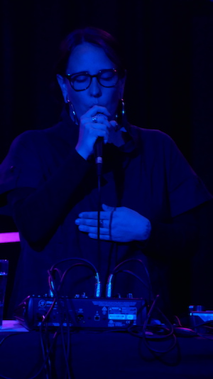 Woman singing into a microphone, lit in blue