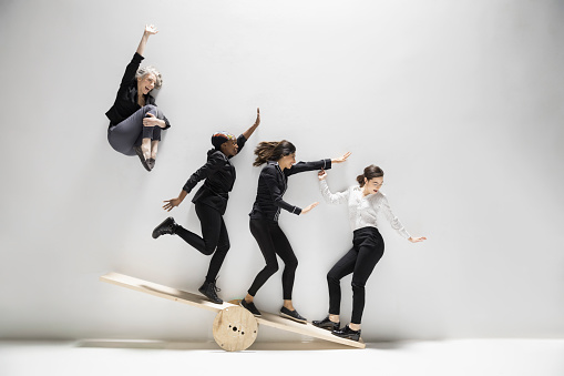 Businesswoman jumping and sliding on seesaw against white background