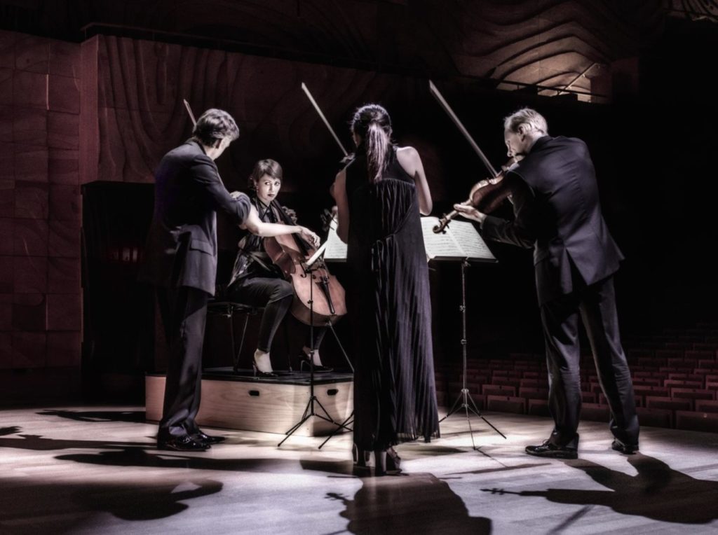 Four performers from a string quartet on stage with their instrument