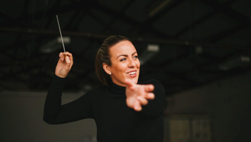 A smiling woman with a baton gestures forwards with her hand