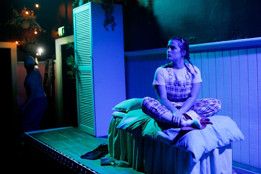 on a stage under blue lights sits a girl on a bed