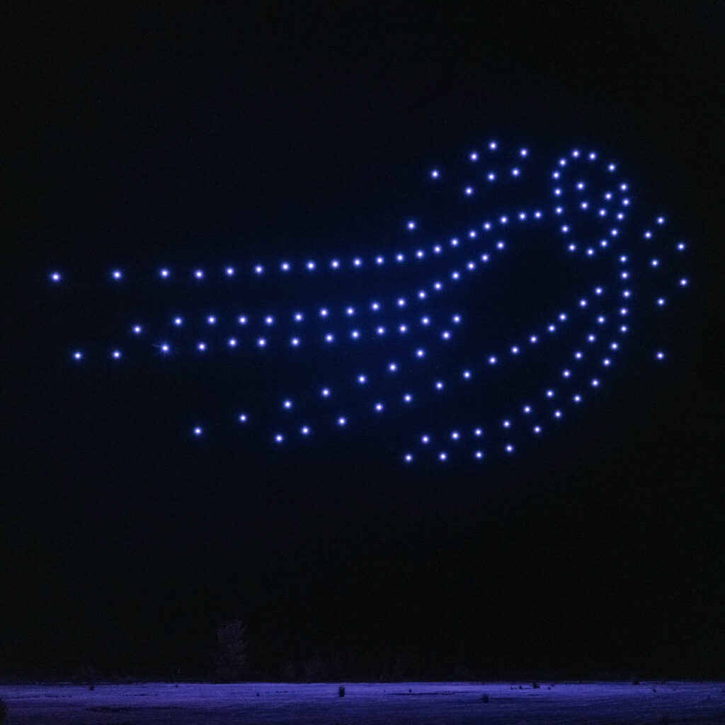 A figure appears in the night sky, composed of blue drone lights