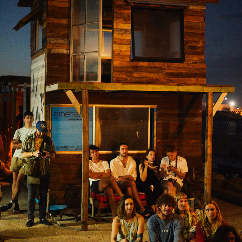 A group of people sitting in front of a two-storey weatherboard house. The look relaxed.