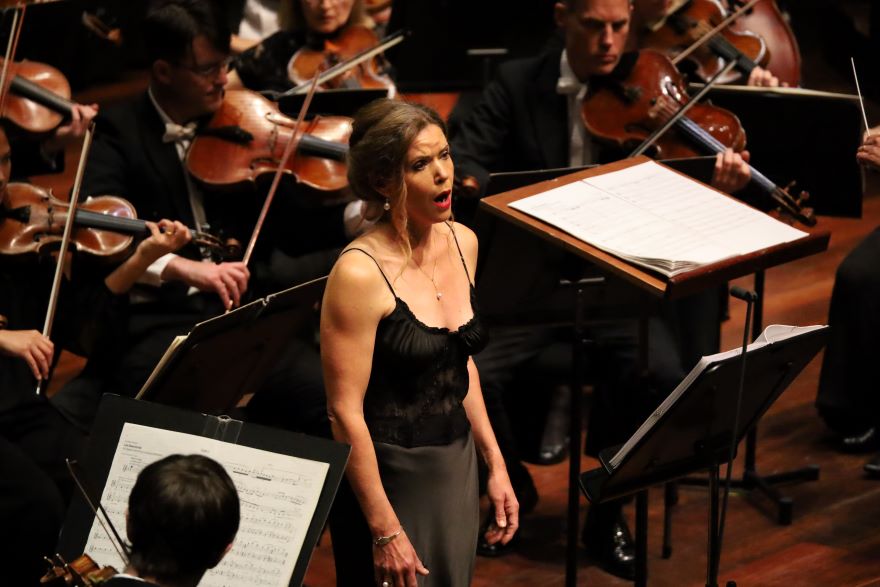 A lady in a black dress sings in front of an orchestera