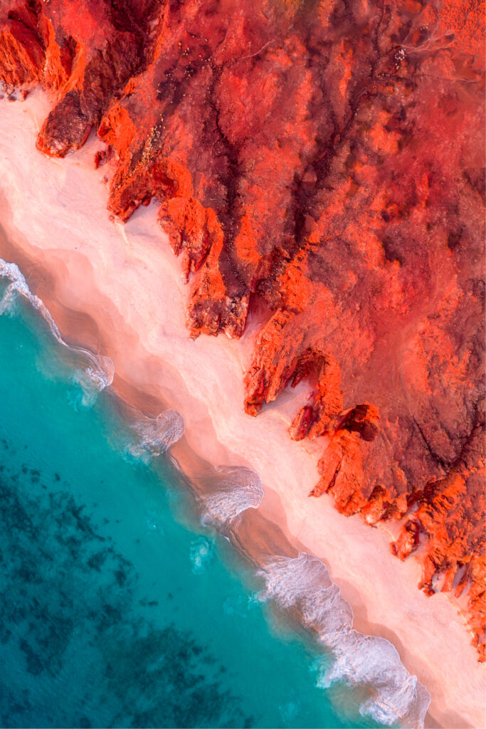 an aerial photo of the vibrant colours of red cliffs at sunset at the blue ocean