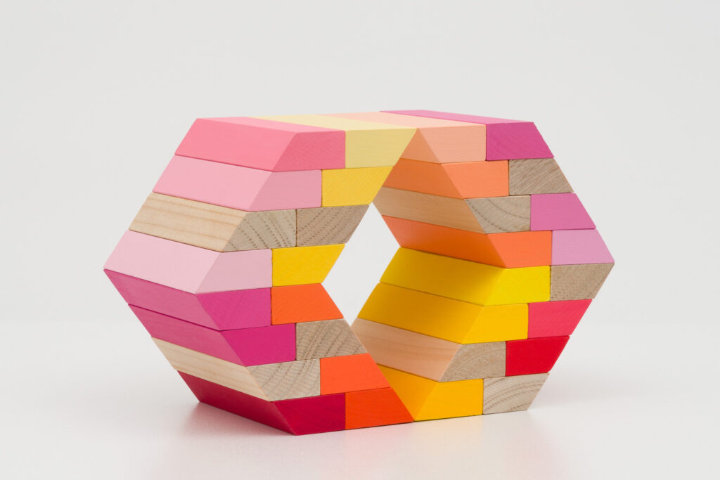 A hexagon shaped sculpture, made of brightly coloured pink, yellow, orange and red bricks.