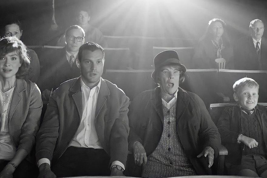 A black and white photo of a lady wearing a hat and coat with two other adults and a child, sitting in cinema chairs with mouths agape