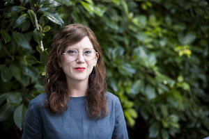 Pictured is the Festival visual arts curator Gemma Weston. She wears an orangey-red lipstick, circular framed glasses and has brown hair with lighter brown highlights.