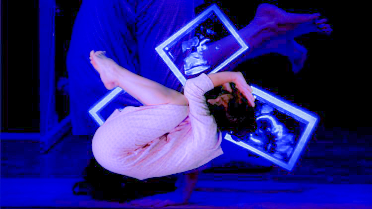 A snapshot ftom the dirty mother, pictured a woman curls up in the foetal position. In the background are blue lit ultrasound pics.