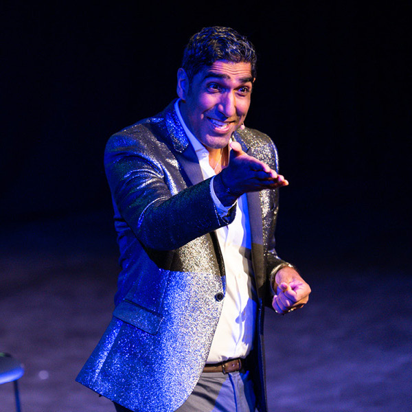 An image from the Fringe show 'Dr Ahmed Gets Hitched'. Pictured is a man gesturing towards the audience with a smile on his face.