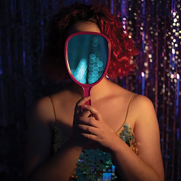 Promotional image from 'Leo/Taurus/Taurus' part of the Summer Nights curation. Pictured is a woman wearing a sequin dress with a red curly bob holds a mirror that conceals her face.