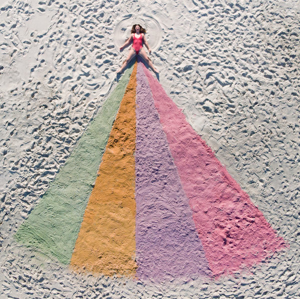 Pictured for Fringe World's show 'My Greatest Period Ever' is a woman in a red one-piece bathing suit lying on some white sand. Below her crotch the sand changes to a rainbow of colours which appear to be coming out of her.