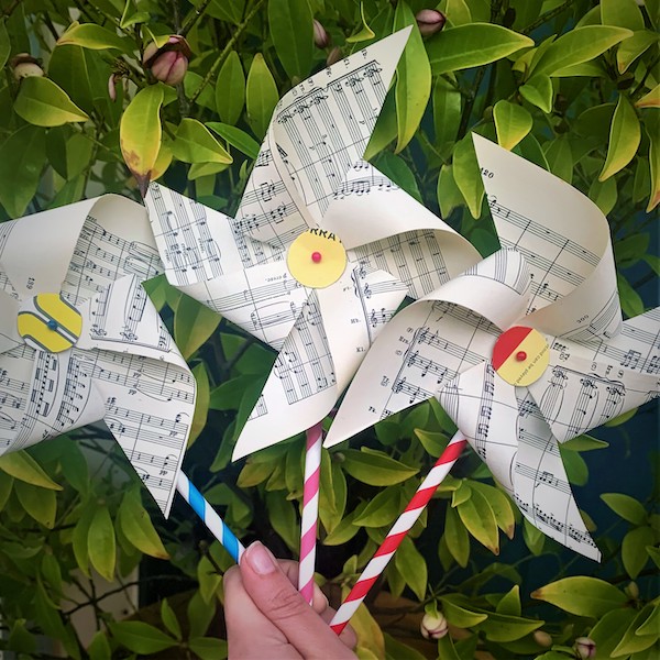 Pictured is three pinwheels made from straws and sheet music in the foreground and a wall of greenery in the background for the Fringe World event 'Djinda Boodja worskshops'.