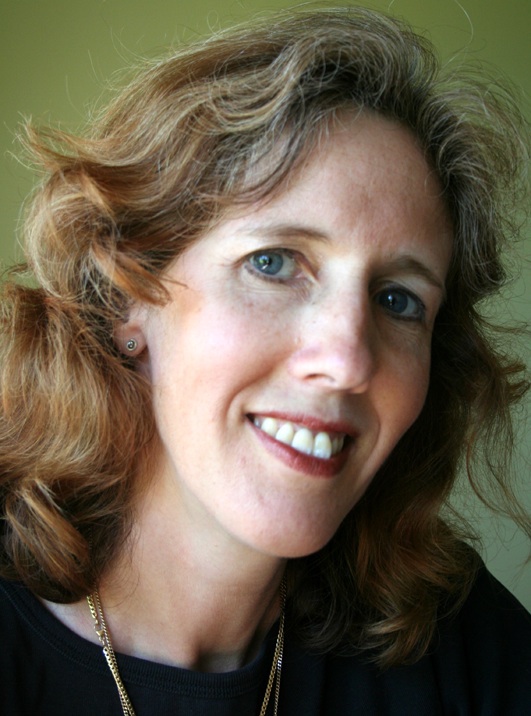 A headshot of Suzanne Inglebrecht the playwright of 2 Marys. She has blonde curly hair streaked with grey and blue eyes and is smiling at the camera.