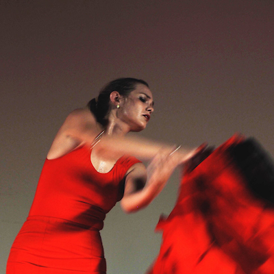 A snapshot from ¡Si! a performance at Fringe World. We see a woman in a red dress in motion. She has a passionate expression on her face.