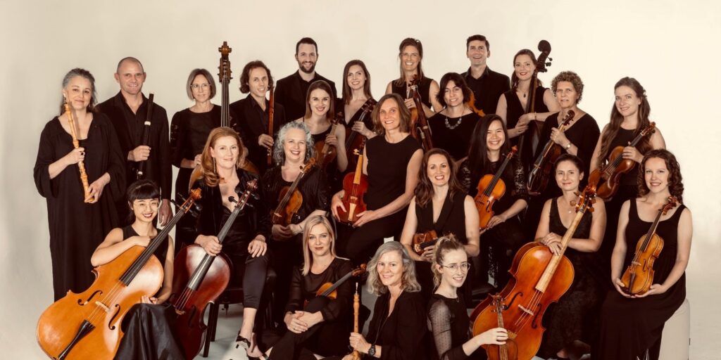 The Australian Baroque made of more than 20 musicians wearing black and holding string instruments, in front of a white studio backdrop