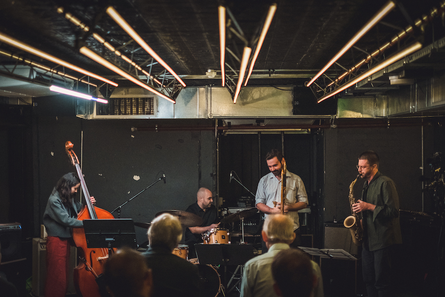 Pictured is jazz quartet 'jalan-jalan' one of two groups headlining TuneNoiseTune. The four jazz musicians play music to a small audience in an industrial room.