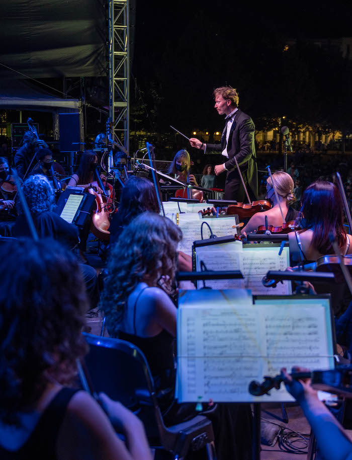 An image of Perth Symphony Orchestra, pictured a conductor stands raised before string players.