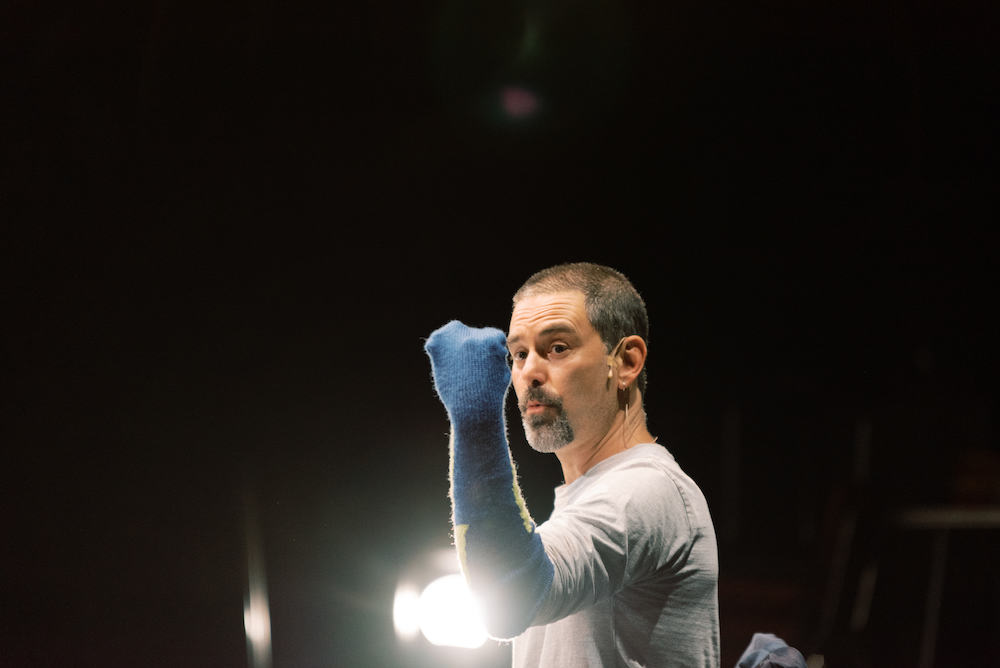 Ben Mortley performs in Kim Crotley's 'The Smallest Stage'. Pictured Mortley holds a blue socked fist up to the camera. He wears a white t-shirt and looks serious, although not aggressive