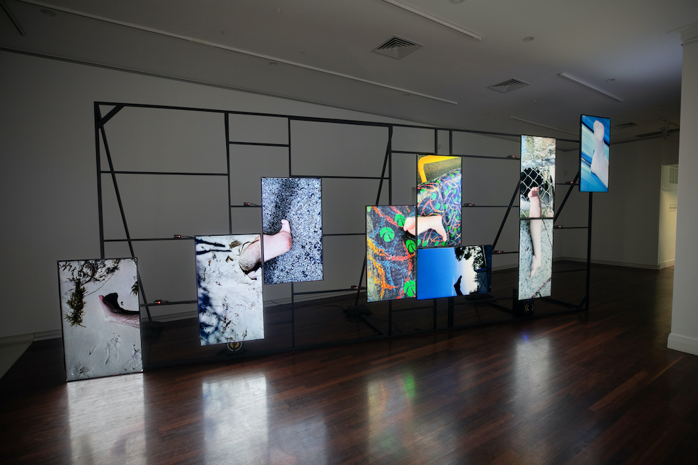 An installation shot of Bruno Booth's Body Shots. Nine screens are placed on a network of frames (almost like a climbing frame), each depicts a different scene.