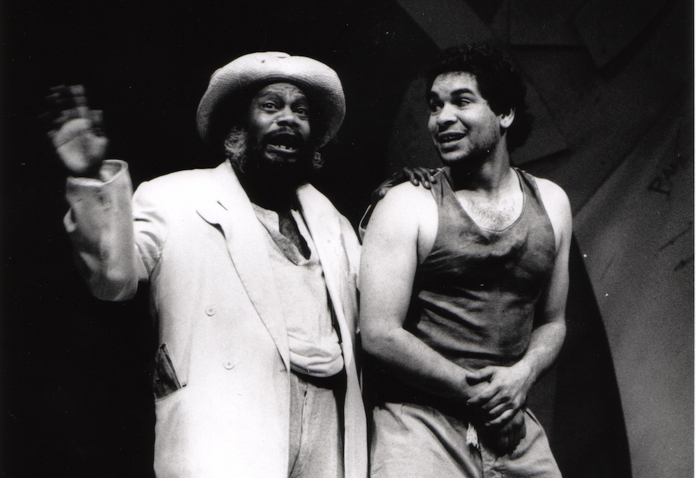 A black and white photo from Twelfth Night directed by Andrew Ross AM. We see two men acting, one wears a singlet the other a coat and top. They hold excited expressions.
