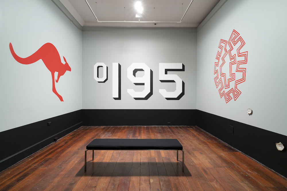A photograph of a room with three walls visible. On one wall is painted a red kangaroo, like the Qantas logo, on another are the numbers "195", with the degree symbol, and the third wall has an abstract red line design.