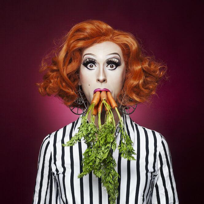Photo shows a woman with five carrots sticking out of her mouth, tops out. 