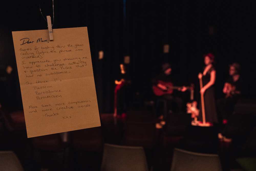 A photograph of a letter is in the foreground. In the background we can discern the performers, although they are out of focus.