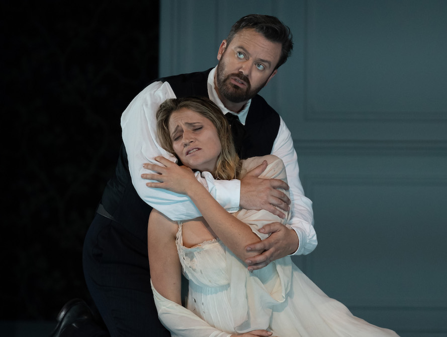 A distraught woman, her dress flimsy and worn, leans into a man's arms. He wraps her tightly, looking into the distance. They are Samantha Clarke and Paul O'Neill in La Traviata.