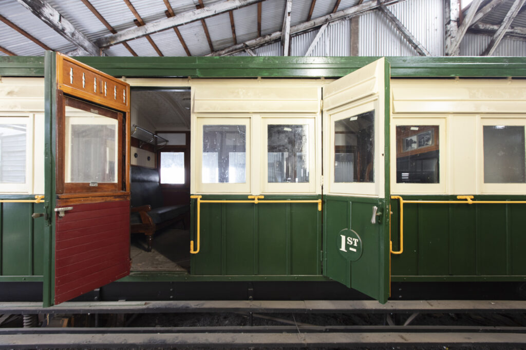 Doors open to an old-fashioned looking train. Painted cream and a rich racing green, with the inside of one door a velvety red. This is one of the exhibits at the South West Rail Museum.