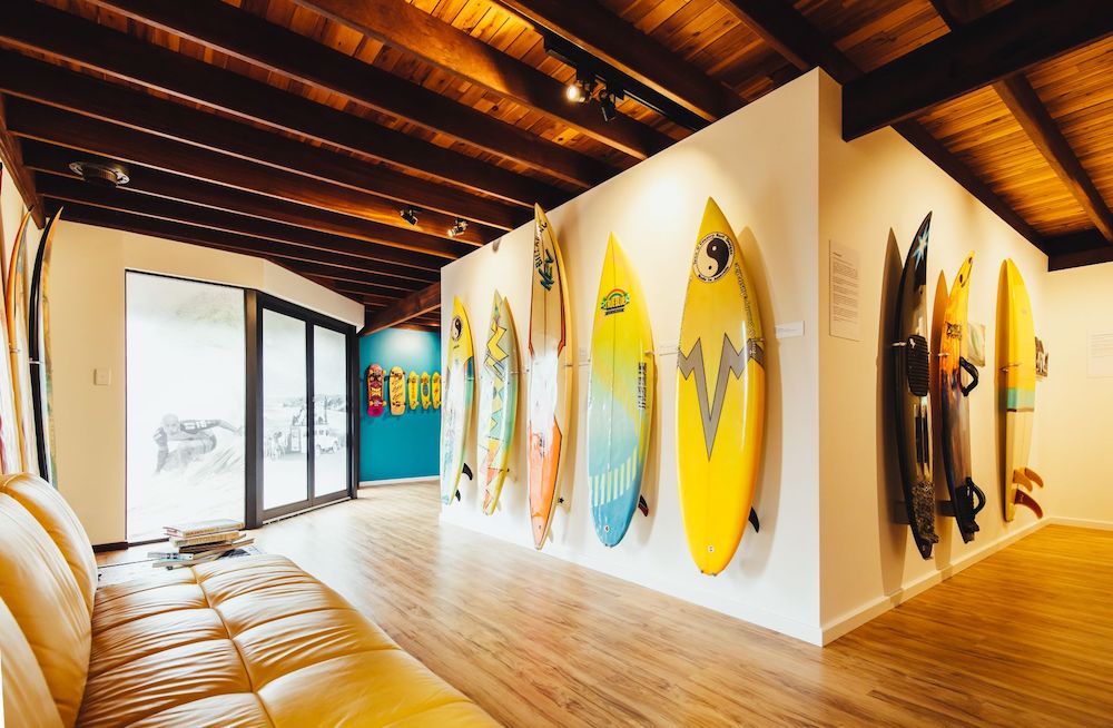 A sunny room with surf boards hanging from the walls. The light is golden against the wooden ceiling beams and floorboards.