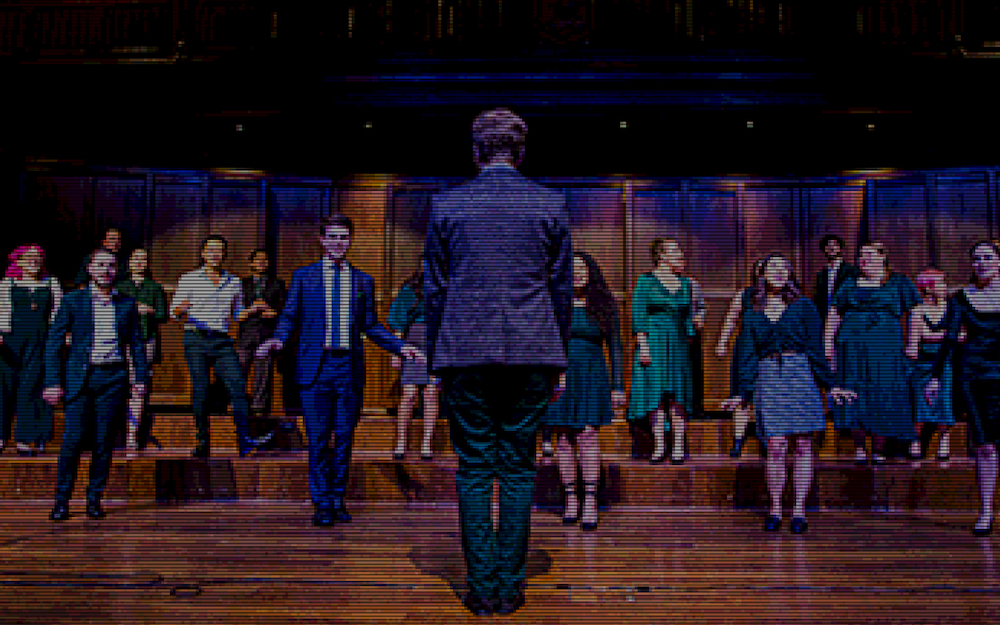 Singers spread out across a stage, facing a conductor who has his back to the camera. The image is pixelated, as if being filtered through an old-fashioned game.
These are the Baden Singers, who are performing at Fringe World.