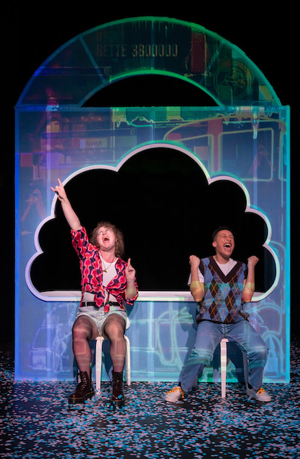 Two people sit in front of a clear frame with a large cutout text cloud. They have triumphant expressions, one is pumping their fists, the other raising one in the air joyfully. 