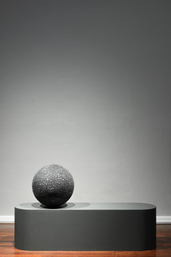 A sphere on a platform. The sphere is covered in what could be hieroglyphics and looks like a small grey moon. 