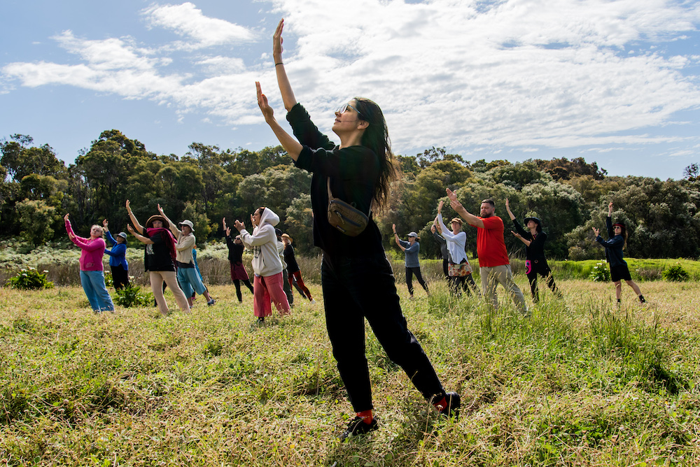 Dancers from The Stars Descend rehearse in a green field, with bushland behind them.