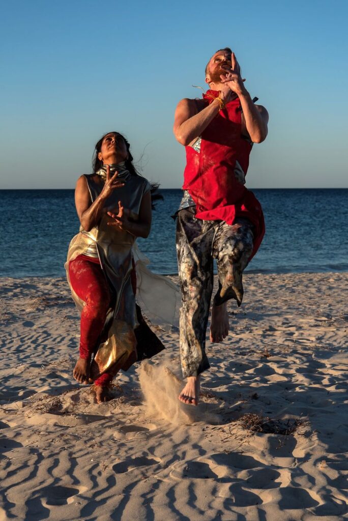 Two dancers from The Stars Descend are on the beach, leaping into the air. 
