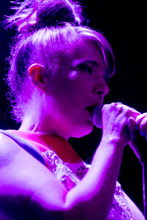 Bikini Kill singer Kathleen Hanna on stage and singing into a a mic.