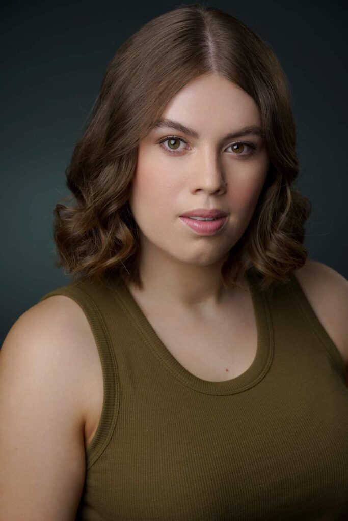 A headshot of a young woman. She is wearing a casual khaki tank top but her hair and makeup suggest this is a serious shot.