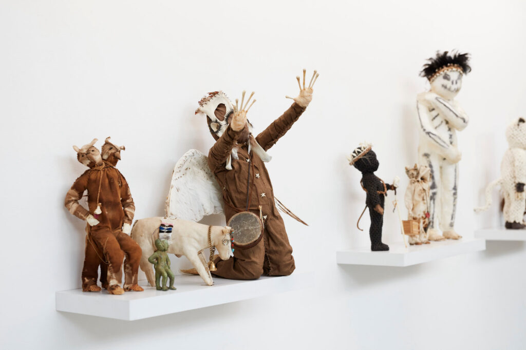 Sculptures of people and animals stand on wall mounted shelves. There is something discomforting about them - one has a stitched mouth like a zombie, another elongated fingers with bulbous tips.