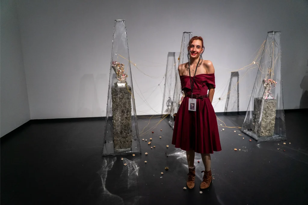 A young woman standing in front of her artwork in a gallery.